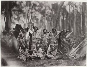 Group of Aborigines, sitting and standing, whole-length, full face, wearing animal skins, some holding weapons. Picture taken by Antoine Fauchery approx. 1857 State Library of Victoria collection